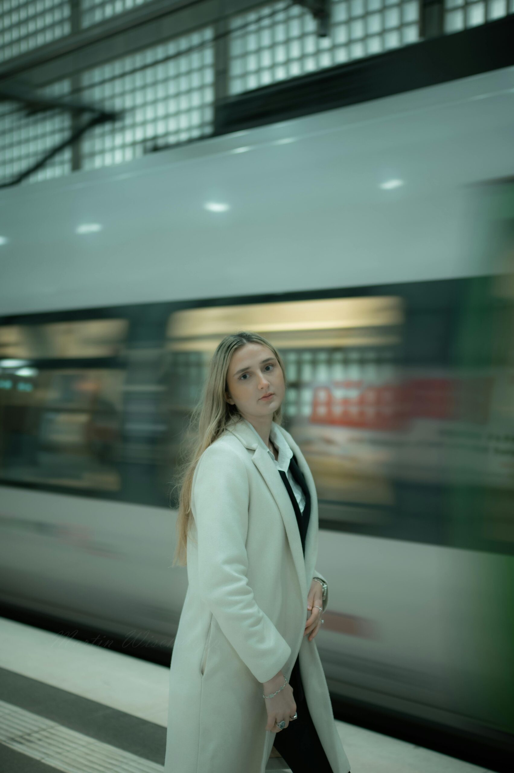 A fashionable woman poses at a bustling train station in Leipzig, showcasing city style.