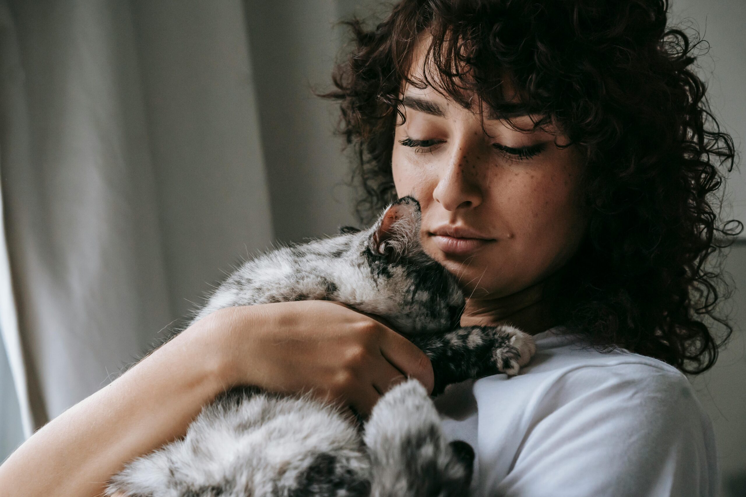 Crop young female with curly hair stroking calm furry cat standing at home
